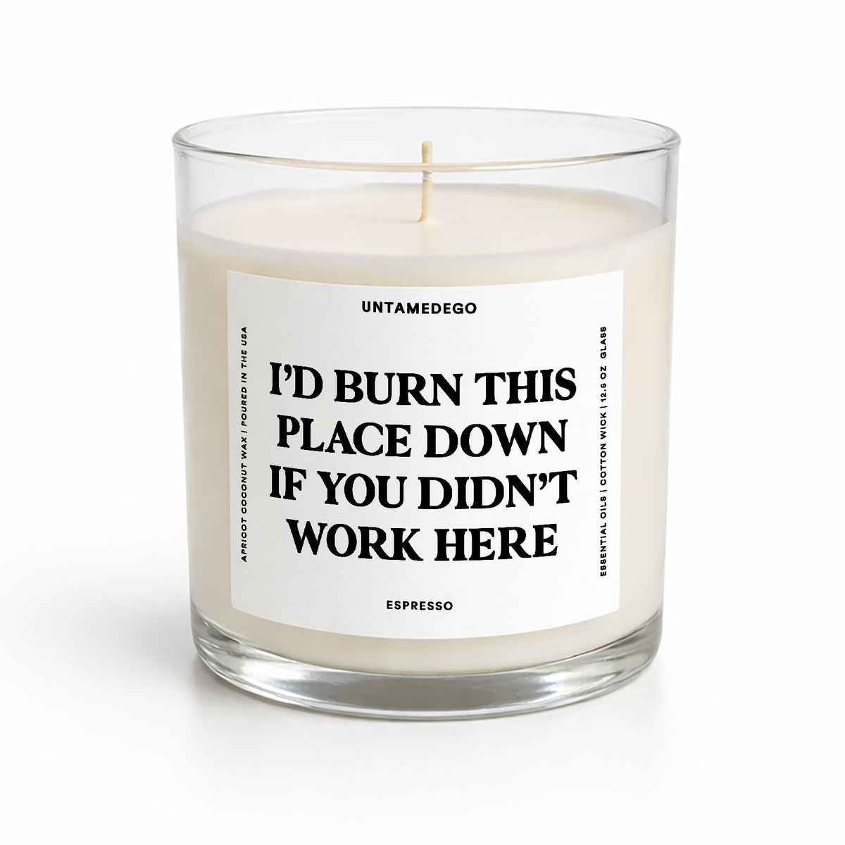 A clear glass jar candle with cream-colored wax and a white label featuring bold black text that reads, 'I'D BURN THIS PLACE DOWN IF YOU DIDN'T WORK HERE.' The brand name 'UNTAMEDEGO' is visible at the top of the label, with 'FEADER FIR' at the bottom.