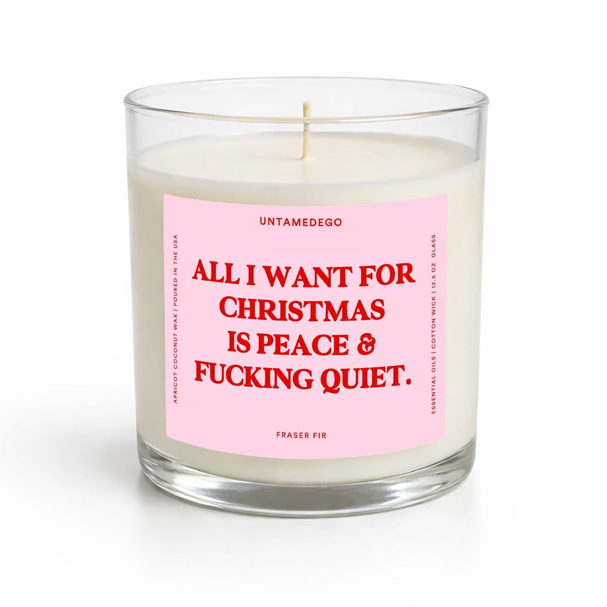 A clear glass jar candle with white wax and a pink label featuring bold red text that reads, 'ALL I WANT FOR CHRISTMAS IS PEACE & FUCKING QUIET.' The brand name 'UNTAMEDEGO' is visible at the top of the label.