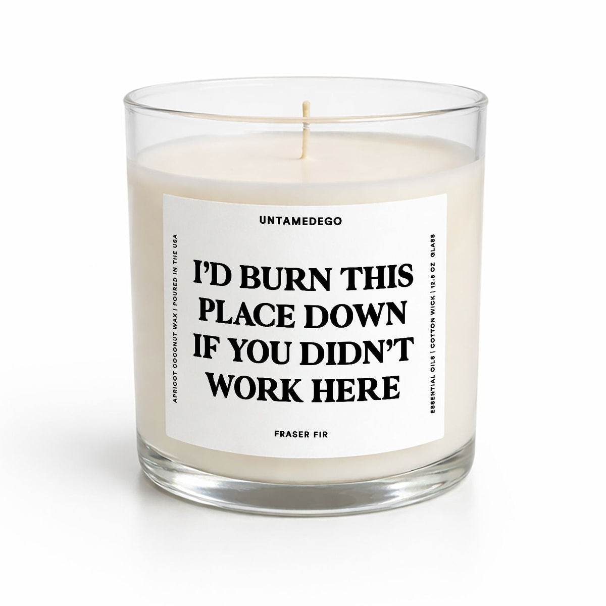 A clear glass jar candle with cream-colored wax and a white label featuring bold black text that reads, 'I'D BURN THIS PLACE DOWN IF YOU DIDN'T WORK HERE.' The brand name 'UNTAMEDEGO' is visible at the top of the label, with 'FEADER FIR' at the bottom.