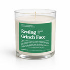 A 16 oz soy wax candle in a clear glass jar with a white wick and a green label that reads 'Resting Fraser Fir Grinch Face' by Unearthed Candles, on a white background.