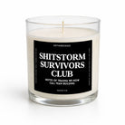 A clear glass jar candle with cream-colored wax and a black label reading 'SHITSTORM SURVIVORS CLUB' in white text, photographed on a clean white background.
