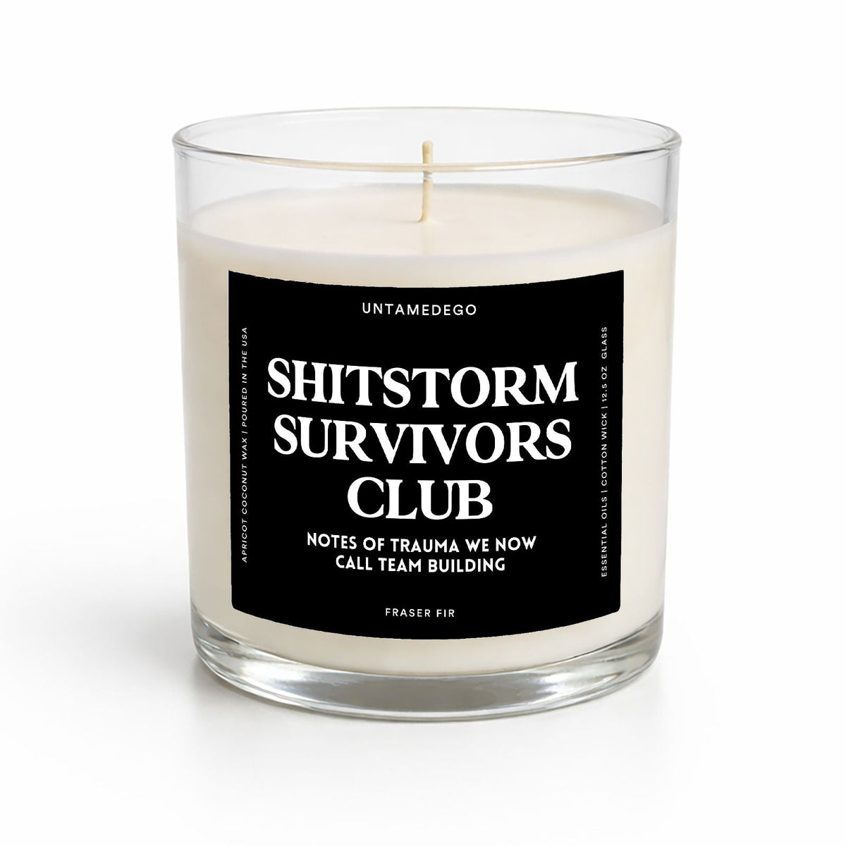 A clear glass jar candle with cream-colored wax and a black label reading 'SHITSTORM SURVIVORS CLUB' in white text, photographed on a clean white background.