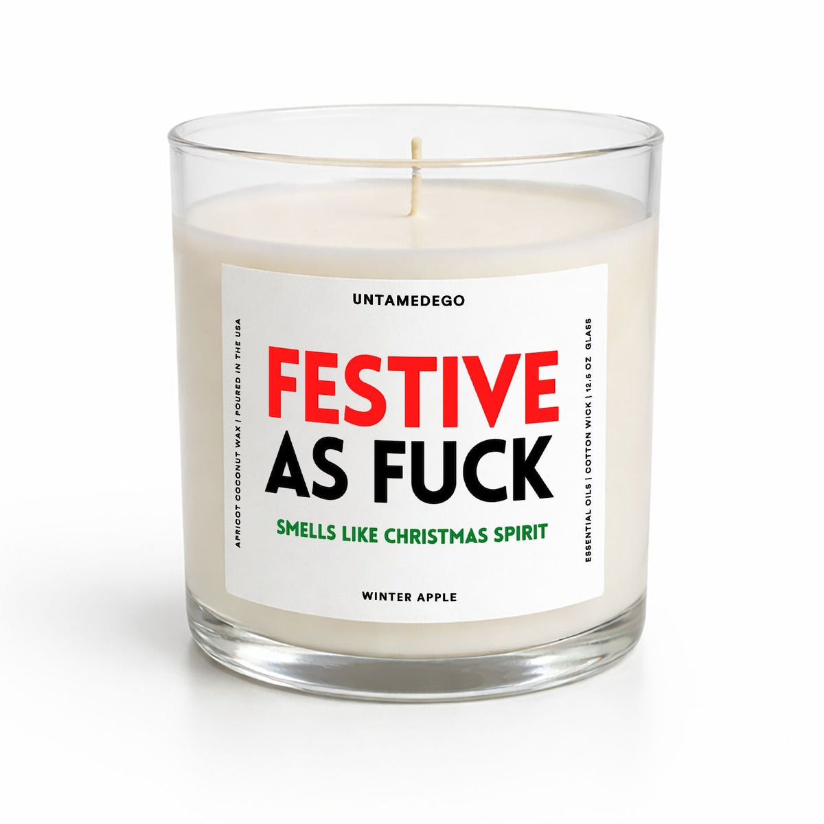 A clear glass jar candle with white wax and a centered white label. The label features the text 'FESTIVE AS FUCK' in red and black, with smaller green and black text below, and 'WINTER APPLE' at the bottom.