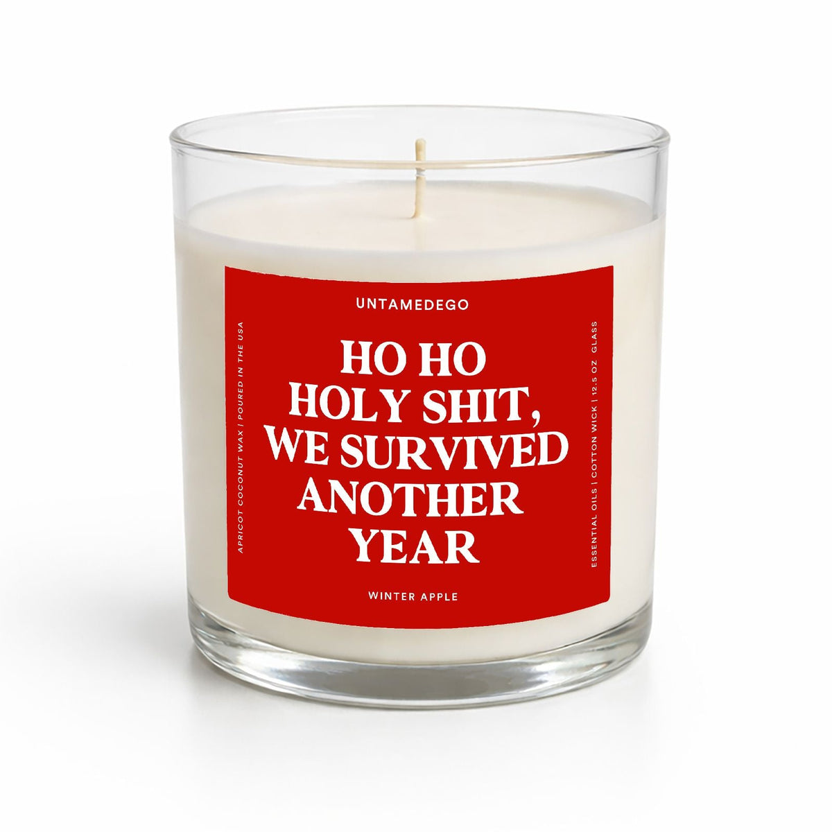 A clear glass jar candle with white wax and a bold red front label reading 'HO HO HOLY SHIT, WE SURVIVED ANOTHER YEAR' in white text. The brand name UNTAMEDOO is visible at the top of the label, and the scent is identified as Winter Apple.