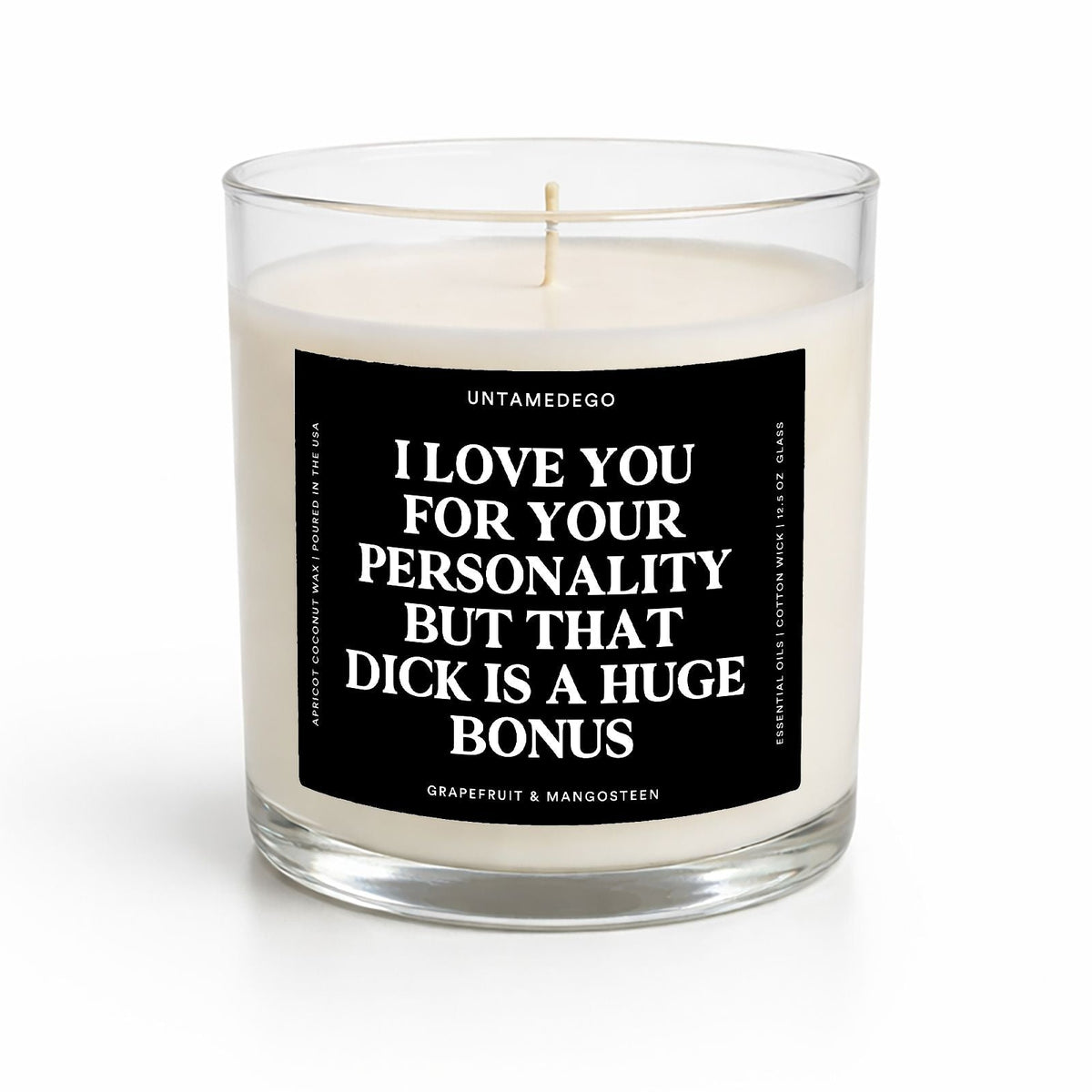 A white soy candle in a clear glass jar with a black square label featuring bold white text that reads, 'I LOVE YOU FOR YOUR PERSONALITY BUT THAT DICK IS A HUGE BONUS.' The candle is photographed on a clean white background with a soft shadow.