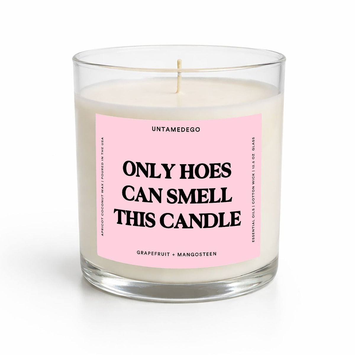 A clear glass jar candle with white wax and a pink label that reads 'ONLY HOES CAN SMELL THIS CANDLE' in bold black text. The brand name 'UNTAMEDEGO' is visible at the top of the label.