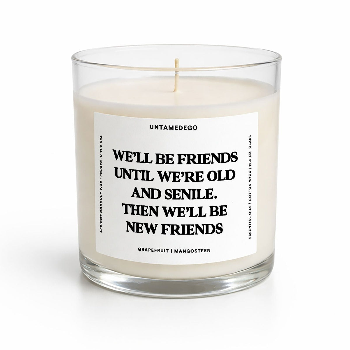 A clear glass jar candle with white wax and a white label featuring black text that reads, 'WE'LL BE FRIENDS UNTIL WE'RE OLD AND SENILE. THEN WE'LL BE NEW FRIENDS.