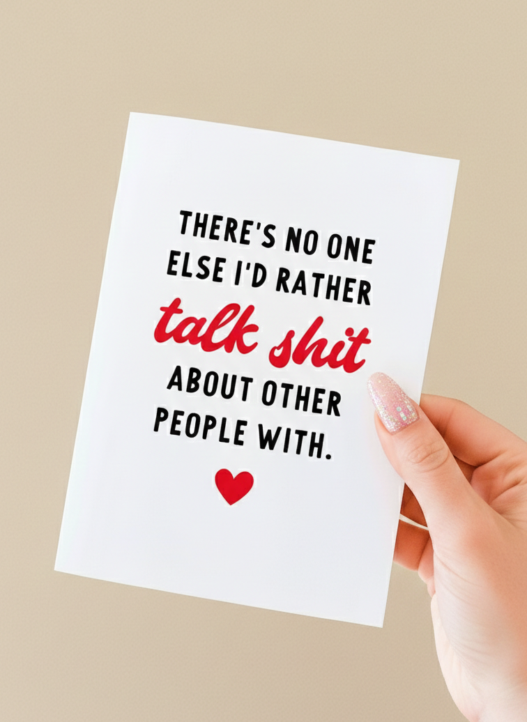 Greeting card held in a hand against a neutral background. The card has a white background with bold black text that reads, “There’s no one else I’d rather,” followed by the phrase “talk shit” in red script-style lettering, and then black text reading, “about other people with.” A small red heart icon appears centered near the bottom of the card. The card is vertically oriented and blank inside
