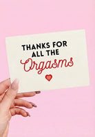 Greeting card with black and red text and a heart graphic on a light pink background, photographed being held by a hand