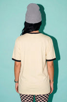 A person shown from the back wearing a cream-colored ringer t-shirt with black trim on the collar and sleeve cuffs, paired with a gray ribbed beanie and black-and-white checkered leggings, set against a solid teal background.