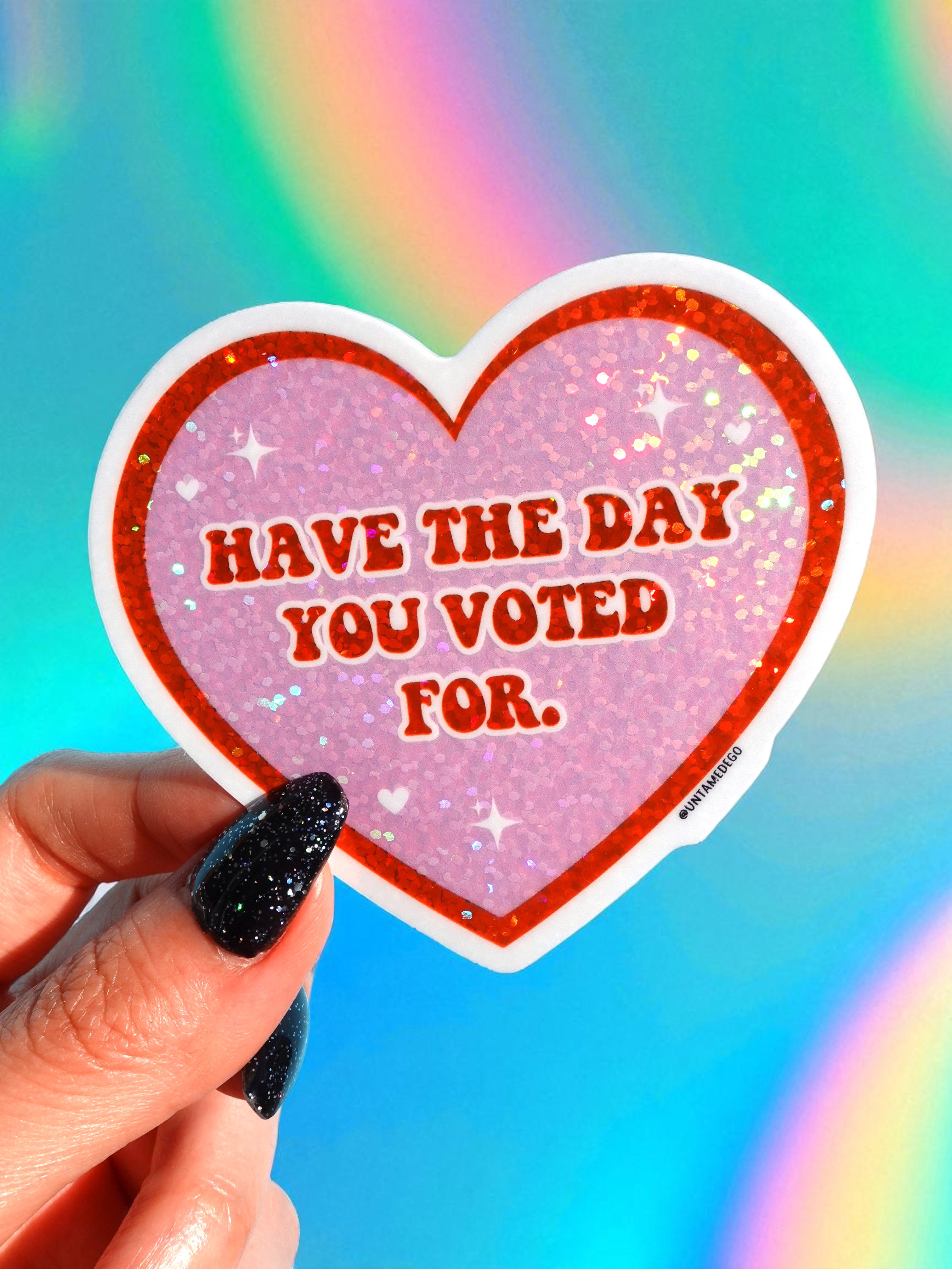 Heart-shaped sticker with 'Have the day you voted for.' text held by a hand against a colorful background