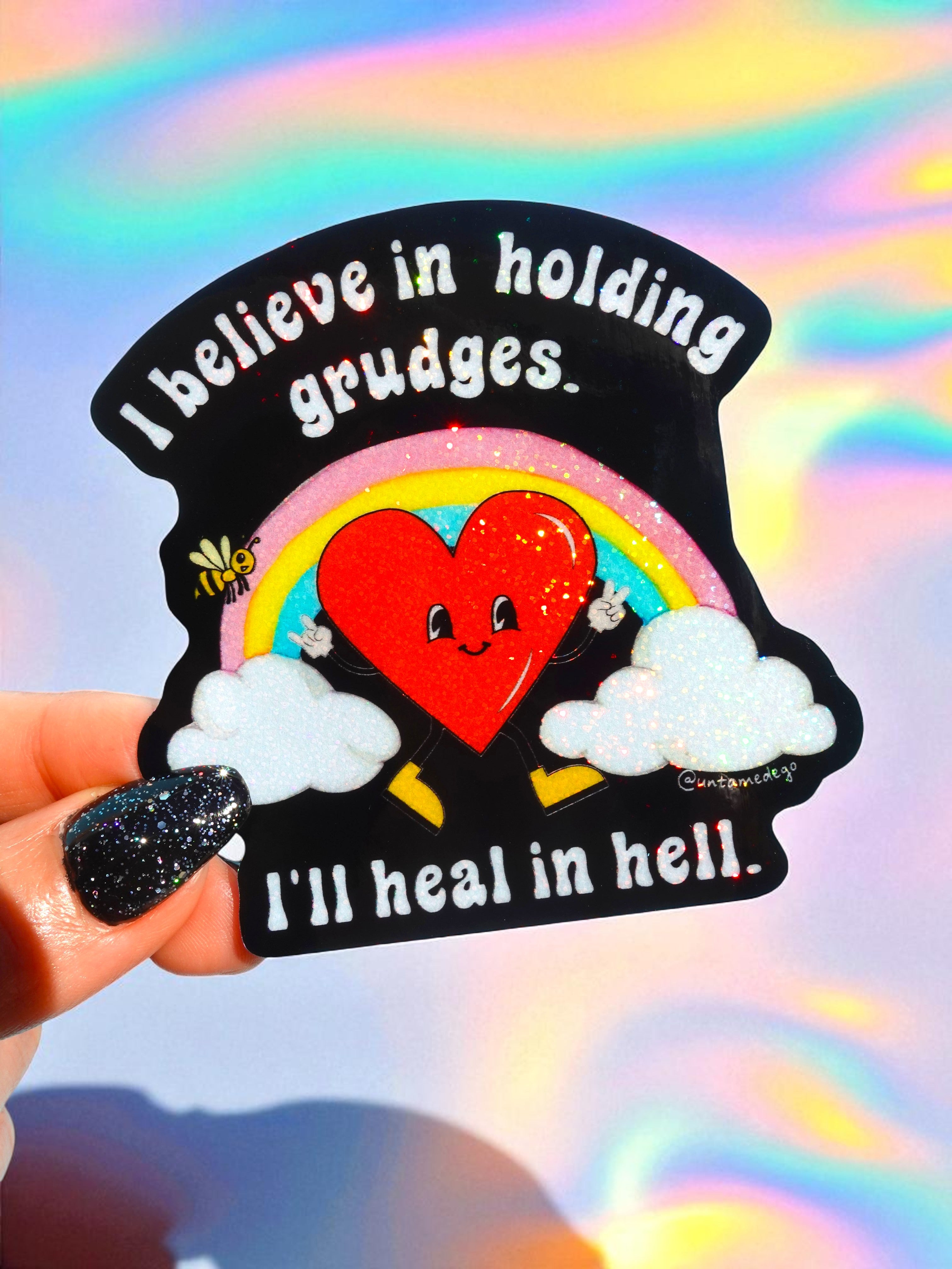 Sticker with rainbow, heart, and text held against a colorful background