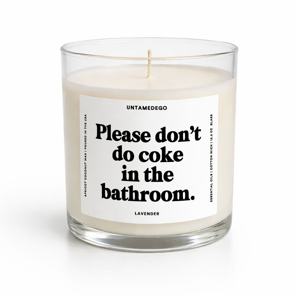 A clear glass jar candle with white wax and a white label featuring bold black text that reads, 'Please don't do coke in the bathroom.' The brand name 'UNTAMEDEGO' is visible at the top of the label, and 'LAVENDER' is printed at the bottom.
