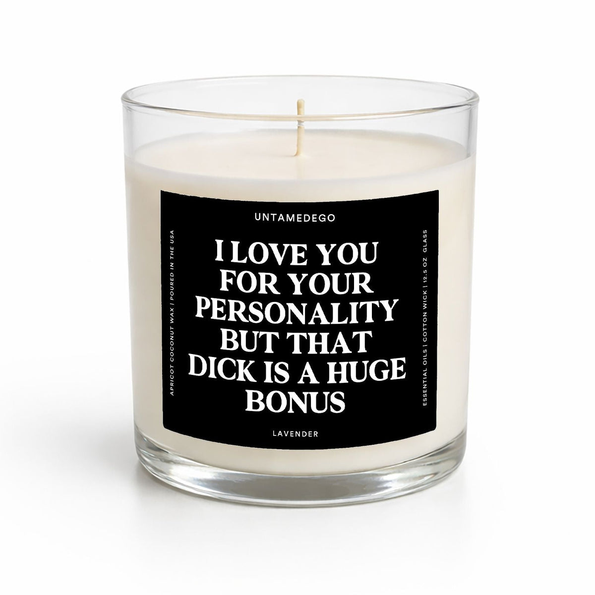 A clear glass jar candle with white wax and a black square label featuring white text that reads, 'I LOVE YOU FOR YOUR PERSONALITY BUT THAT DICK IS A HUGE BONUS.' The label also shows the brand name 'UNTAMEDEGO' and the scent 'LAVENDER.