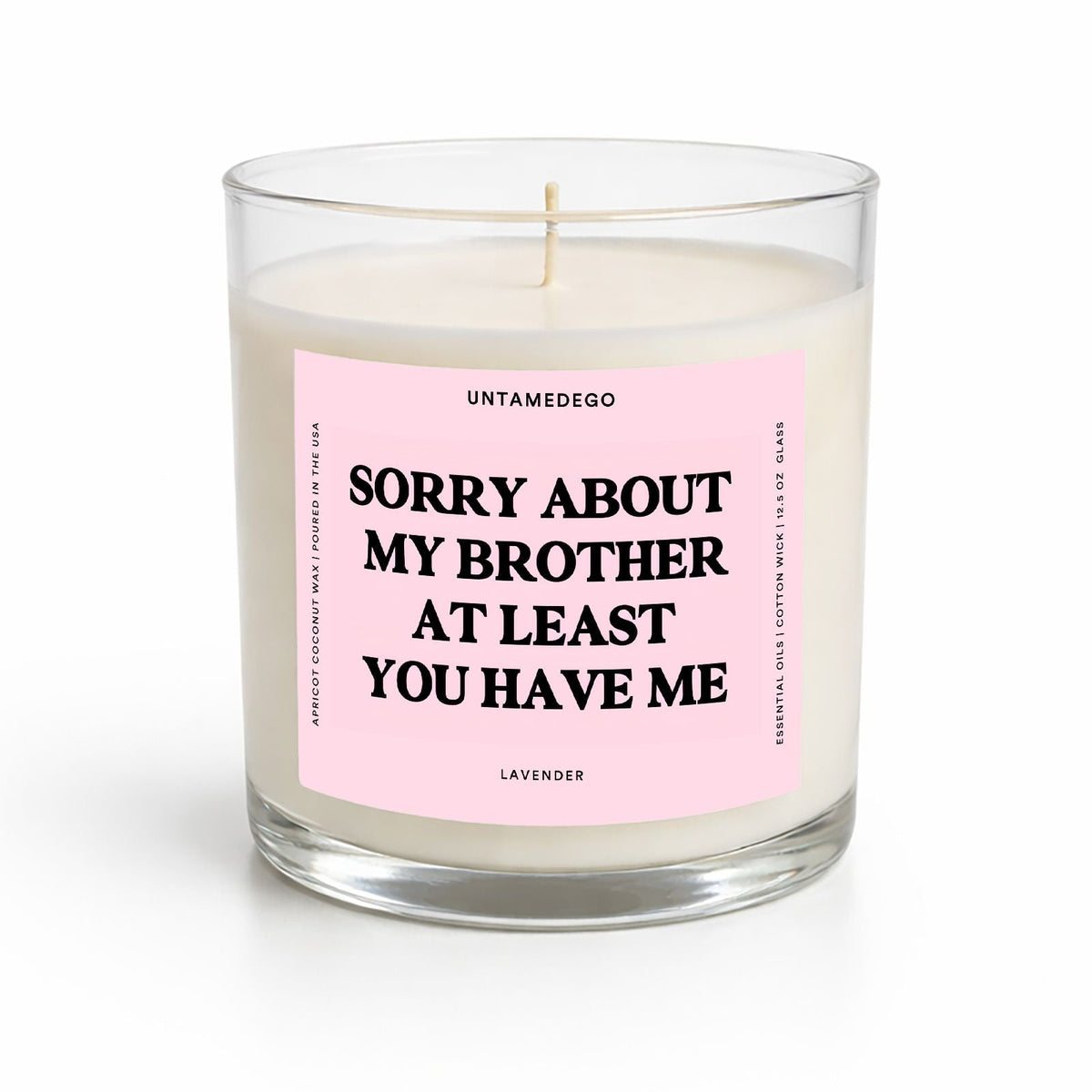 A clear glass jar candle with white wax and a pink label that reads 'SORRY ABOUT MY BROTHER AT LEAST YOU HAVE ME' in black text. The brand name 'UNTAMEDEGO' is visible at the top of the label.