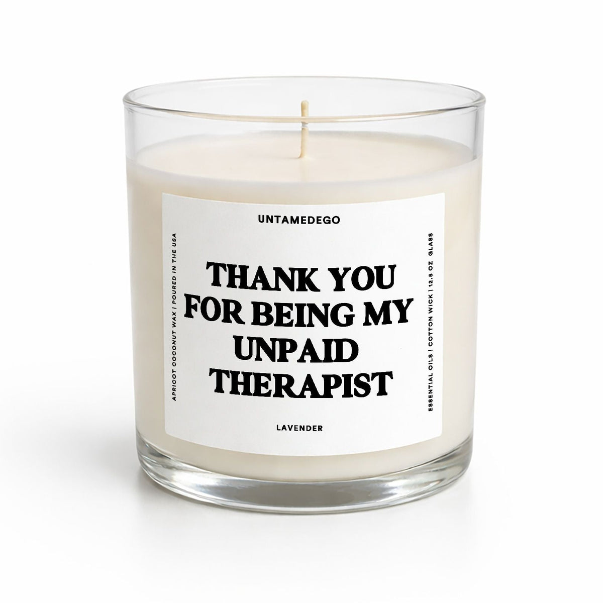 A clear glass jar candle with white wax and a white label featuring bold black text that reads 'THANK YOU FOR BEING MY UNPAID THERAPIST' and 'UNTAMEDOGO' at the top, on a clean white background.