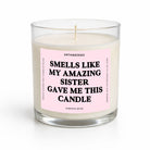 A glass jar candle with white wax and a pink label that reads 'SMELLS LIKE MY AMAZING SISTER GAVE ME THIS CANDLE' by Untamedgo, shown on a white background.