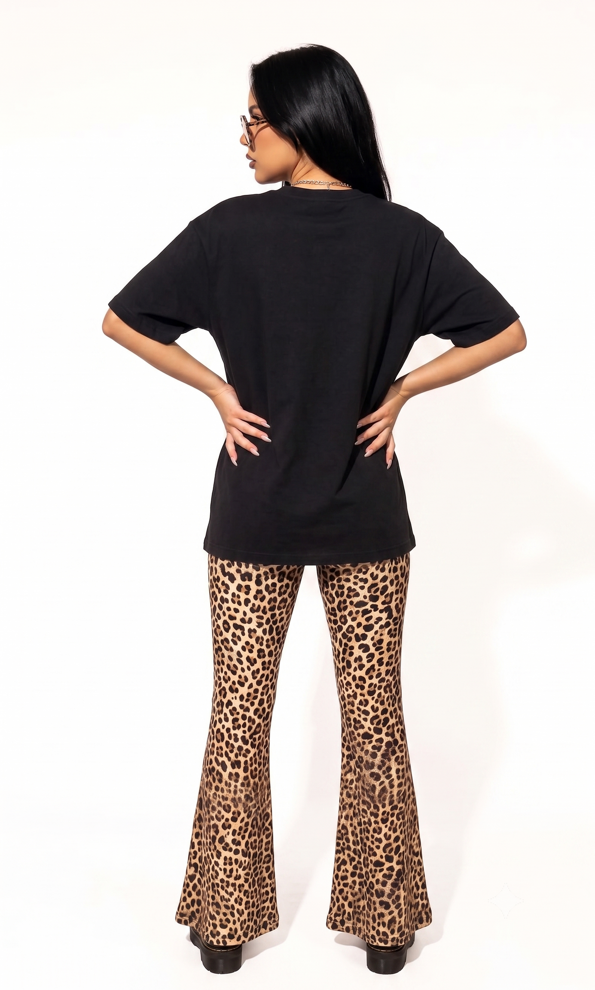 A woman shown from the back wearing a black oversized short-sleeve t-shirt and leopard print flared pants, standing against a plain white studio background.