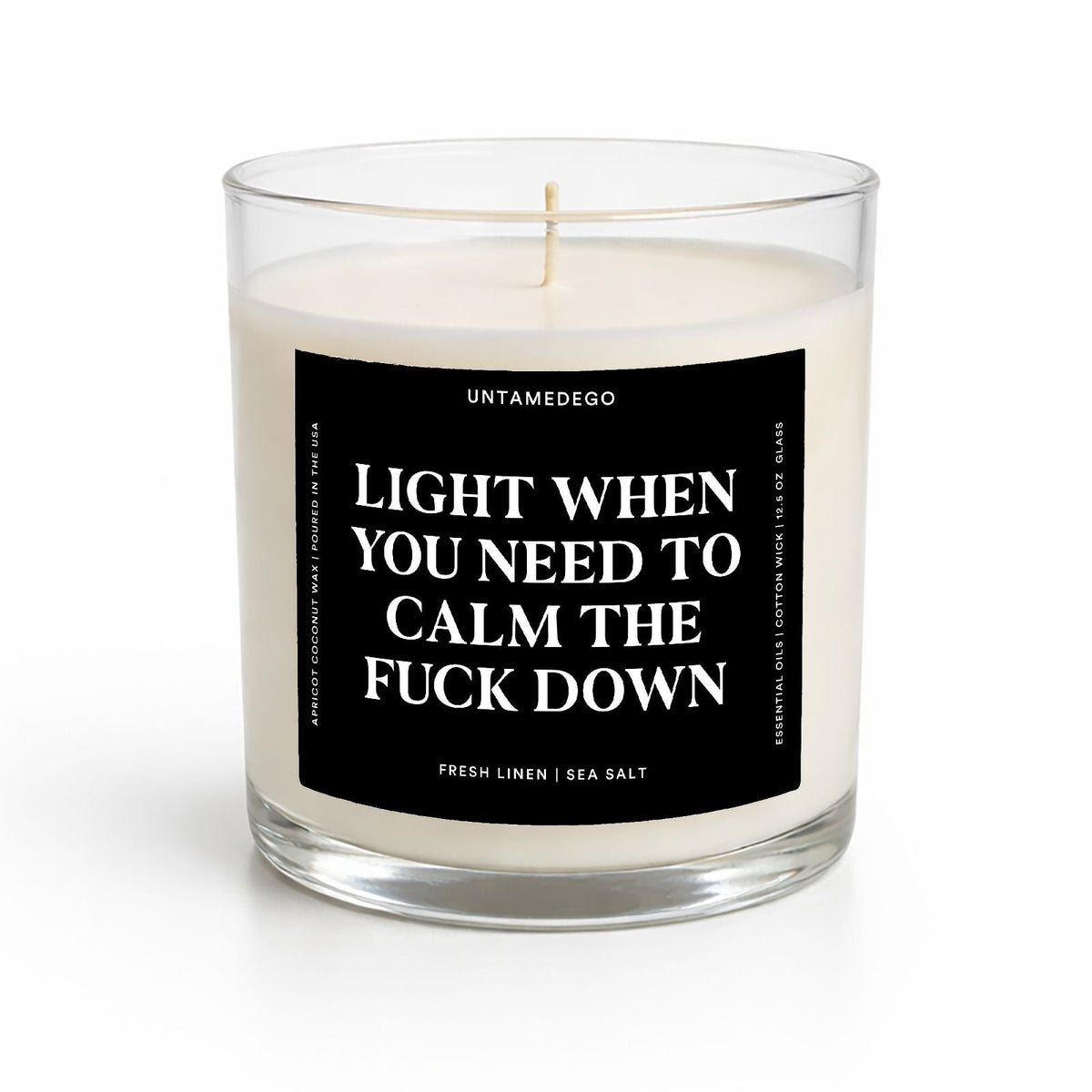 A clear glass jar candle with white wax and a black front label featuring bold white text that reads, 'LIGHT WHEN YOU NEED TO CALM THE FUCK DOWN' with the brand name 'UNTAMEDEGO' above. The candle is photographed on a clean white background.