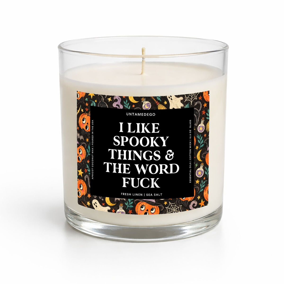 A clear glass jar candle with white wax and a single wick, featuring a black front label with white text that reads 'I LIKE SPOOKY THINGS & THE WORD FUCK' and a colorful Halloween-themed border with pumpkins, ghosts, and spiders. The candle is photographed on a clean white background.