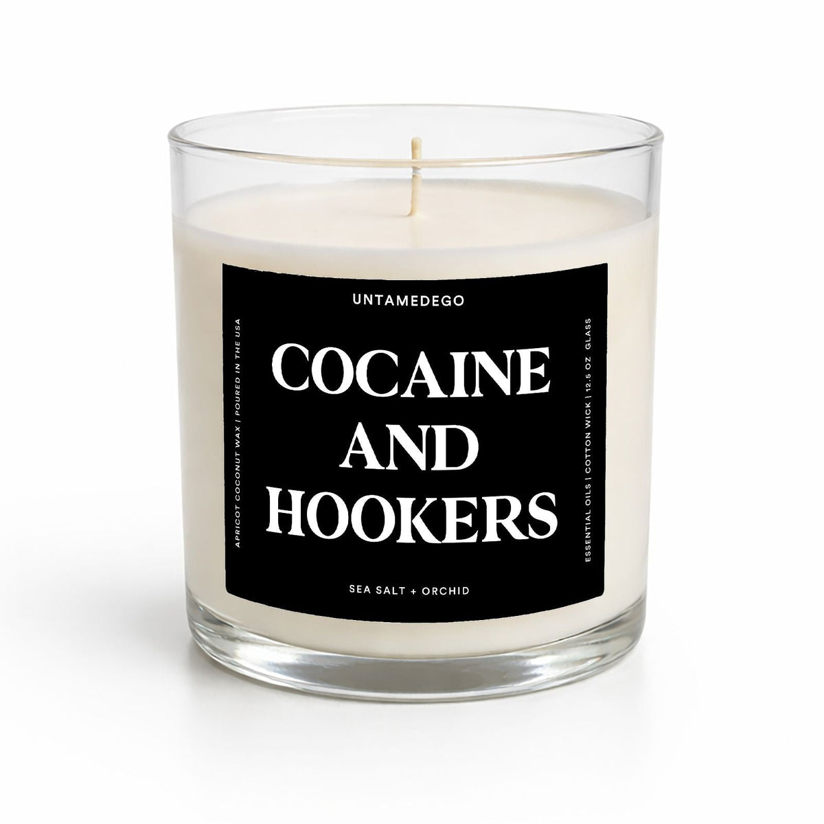 A clear glass jar candle with white wax and a black label reading 'COCAINE AND HOOKERS' in white text, photographed on a clean white background.