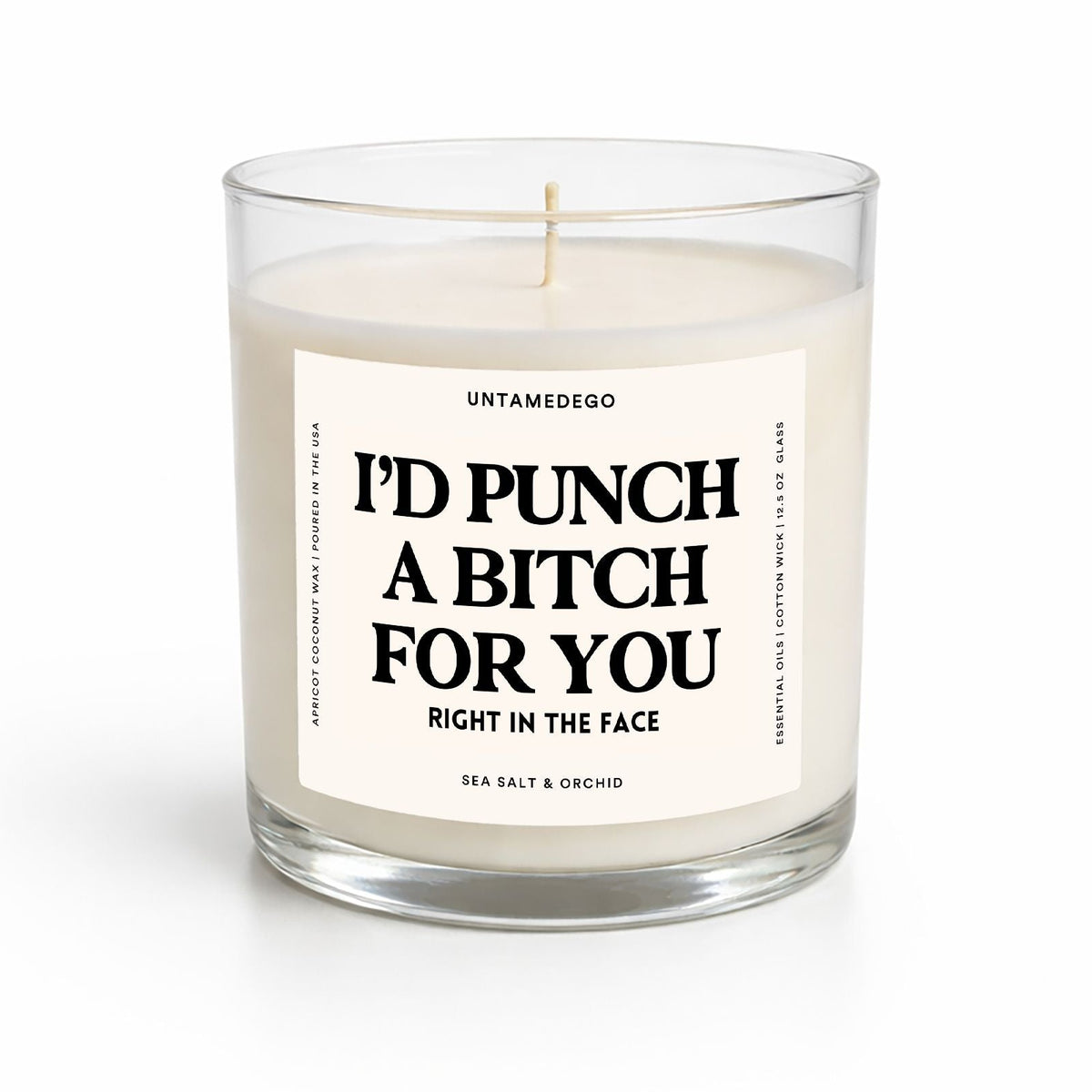 A sea salt and orchid scented candle in a clear glass jar with a white label that reads 'I'D PUNCH A BITCH FOR YOU RIGHT IN THE FACE' by Untamedigo.