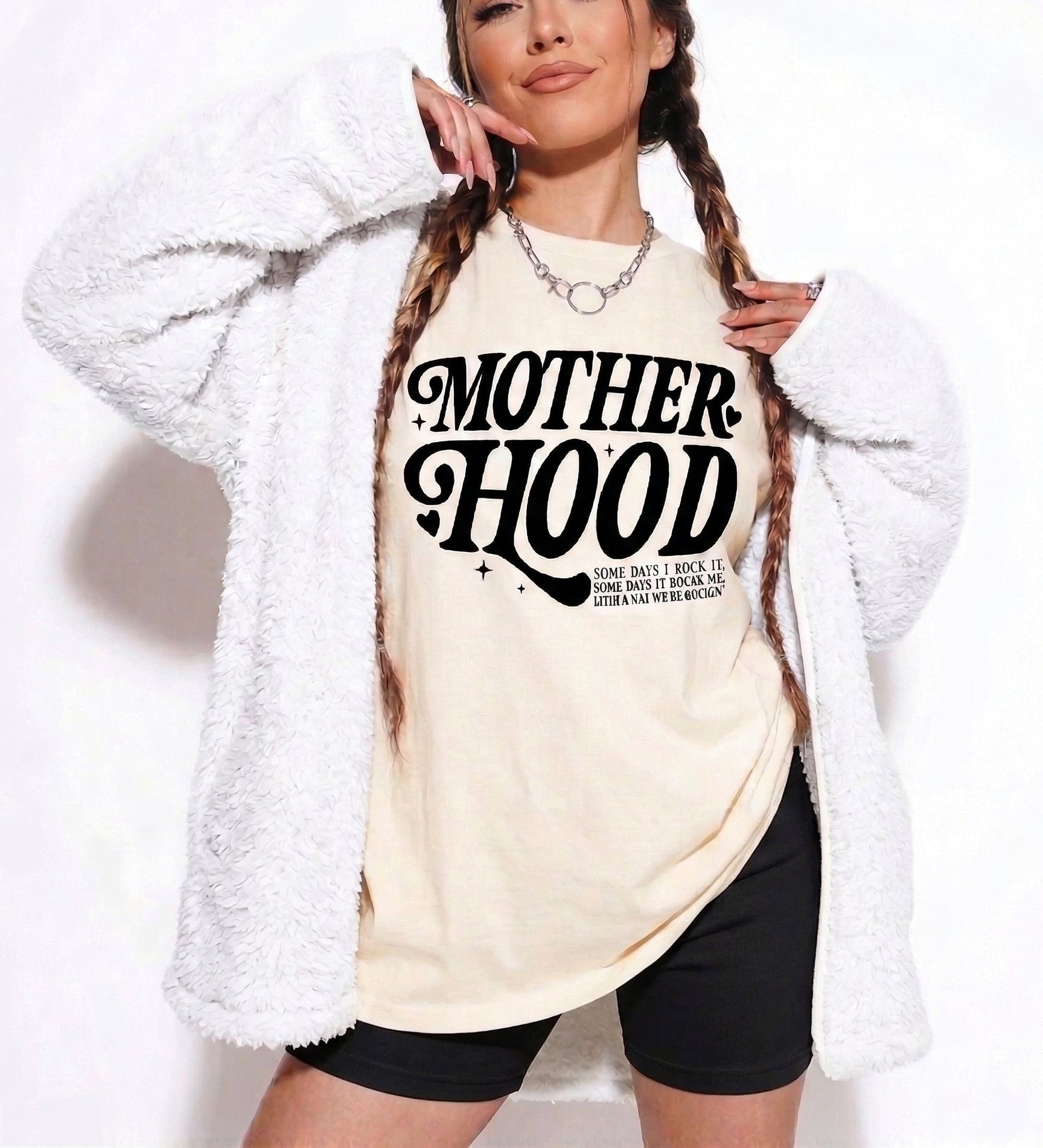 Woman wearing a white t-shirt with 'MOTHERHOOD' text, standing against a plain background