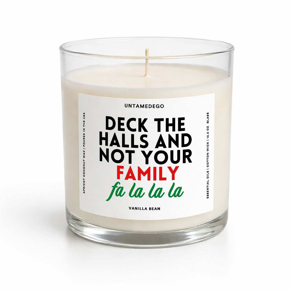 A single-wick candle in a clear glass jar with cream-colored wax and a white label that reads 'UNTAMEDEGO DECK THE HALLS AND NOT YOUR FAMILY fa la la la' in black, red, and green text, on a white background.