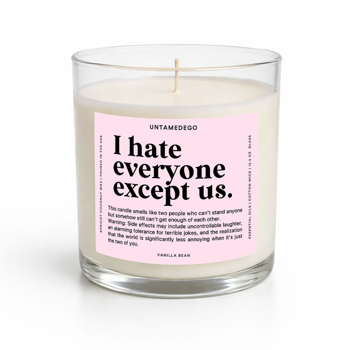 A clear glass jar candle with white wax and a pink label reading 'I hate everyone except us.' by UNTAMEDEGO, shown on a clean white background.