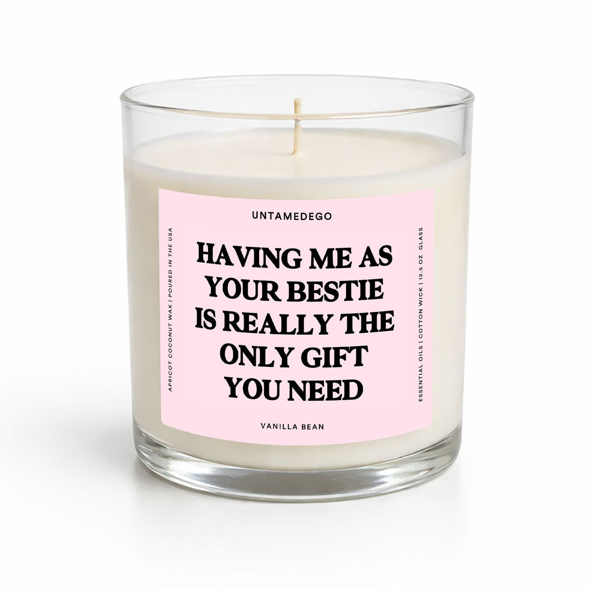 A single-wick candle in a clear glass jar with cream-colored wax and a light pink label featuring bold black text that reads, 'HAVING ME AS YOUR BESTIE IS REALLY THE ONLY GIFT YOU NEED.' The label also shows the brand name 'UNTAMEDEGO' and scent 'VANILLA BEAN.