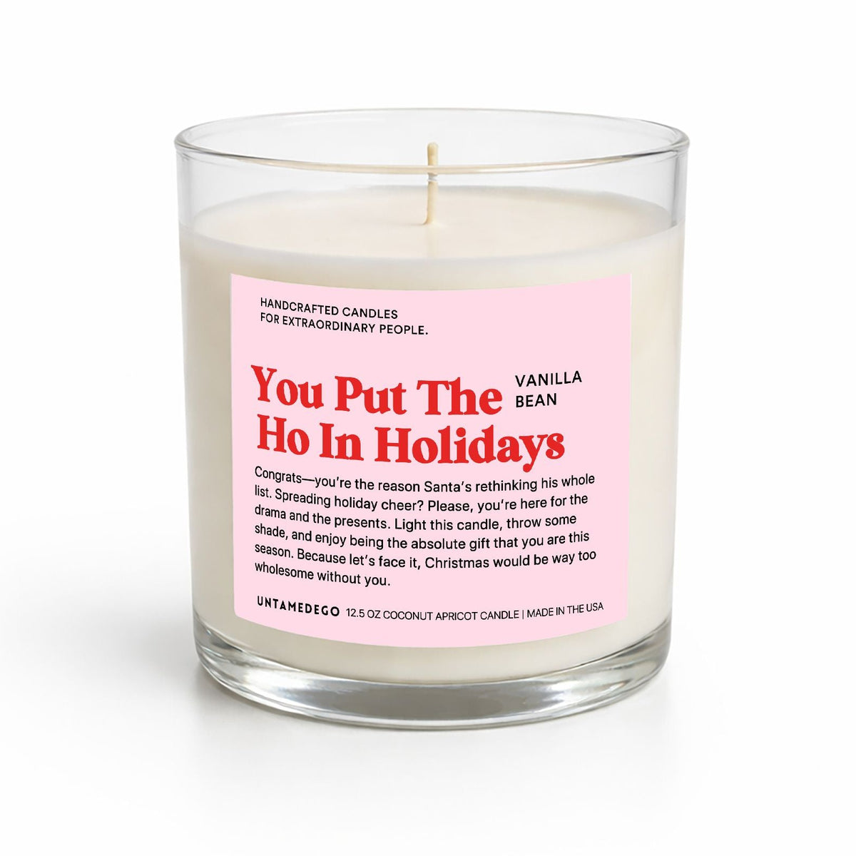 A handcrafted soy candle in a clear glass jar with a white wax fill and a pink label that reads 'You Put The Ho In Holidays' and 'Vanilla Bean'.