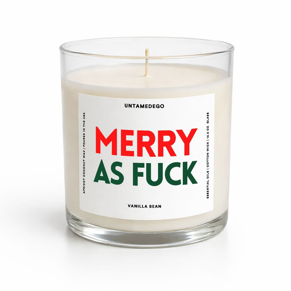 A clear glass jar candle with white wax and a white label reading 'MERRY AS FUCK' in red and green, with 'UNTAMEDEGO' and 'VANILLA BEAN' in smaller black text, on a white background.