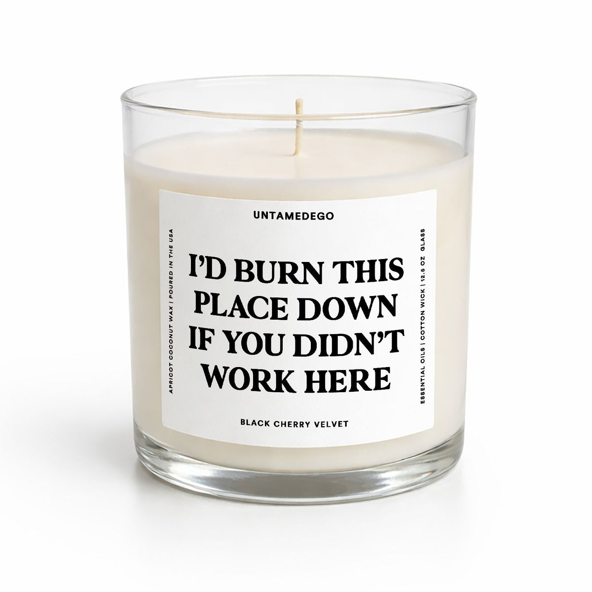A clear glass jar candle with cream-colored wax and a white label featuring bold black text that reads, 'I'D BURN THIS PLACE DOWN IF YOU DIDN'T WORK HERE.' The brand name 'UNTAMEDEGO' is visible at the top of the label.