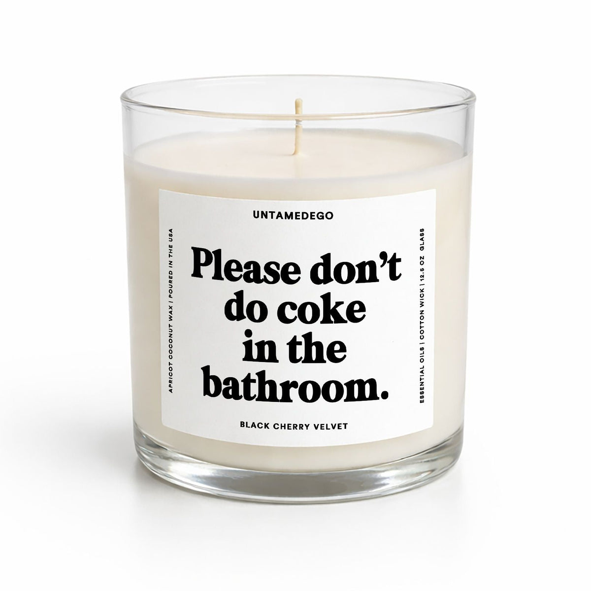 A single-wick soy candle in a clear glass jar with a white label that reads 'Please don't do coke in the bathroom.' by UNTAMEDGO, shown on a clean white background.