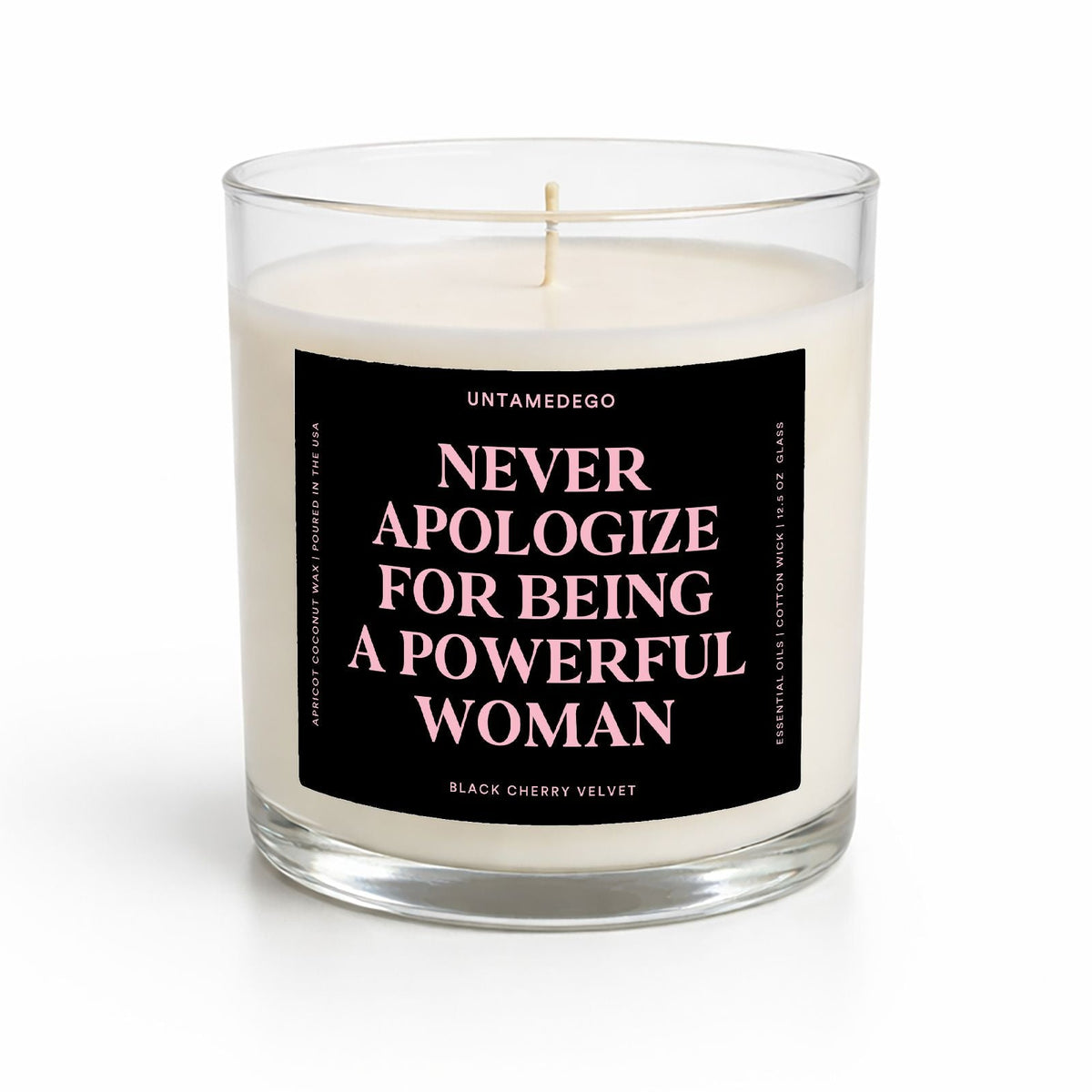 A clear glass jar candle with white wax and a black label featuring pink text that reads 'NEVER APOLOGIZE FOR BEING A POWERFUL WOMAN' by Untamedogo.