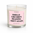 A clear glass jar candle with white wax and a pink label that reads 'SMELLS LIKE SHE'S READING SMUT AGAIN' by Untamedgo, shown on a clean white background.