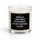 A clear glass jar candle with white wax and a black label featuring white text that reads 'SMELLS LIKE SHE'S WATCHING SCARY MOVIES AGAIN' and the brand name 'UNTAMEDEGO'.