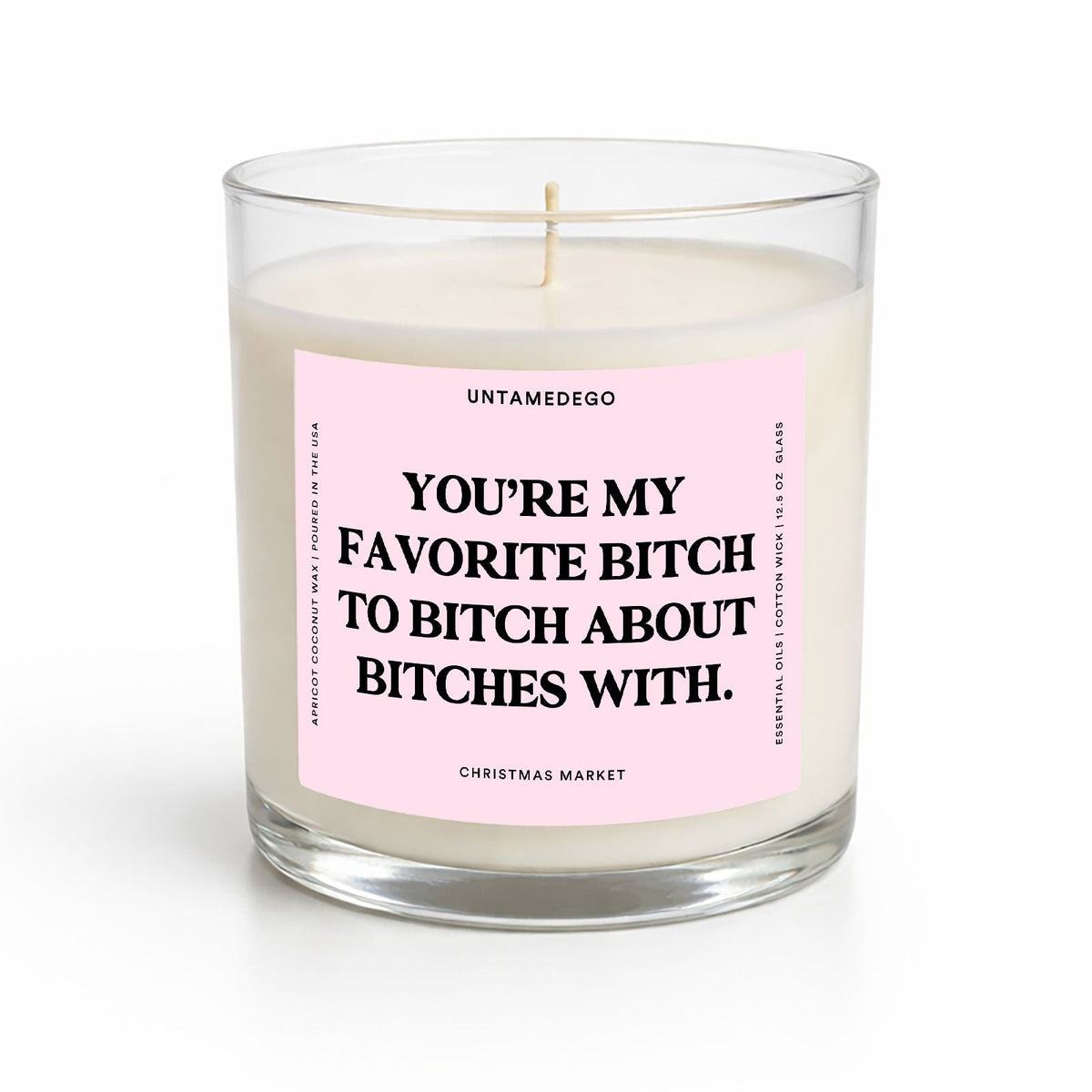 A clear glass jar candle with white wax and a pink front label featuring bold black text. The label reads 'UNTAMEDEGO' at the top and 'CHRISTMAS MARKET' at the bottom.