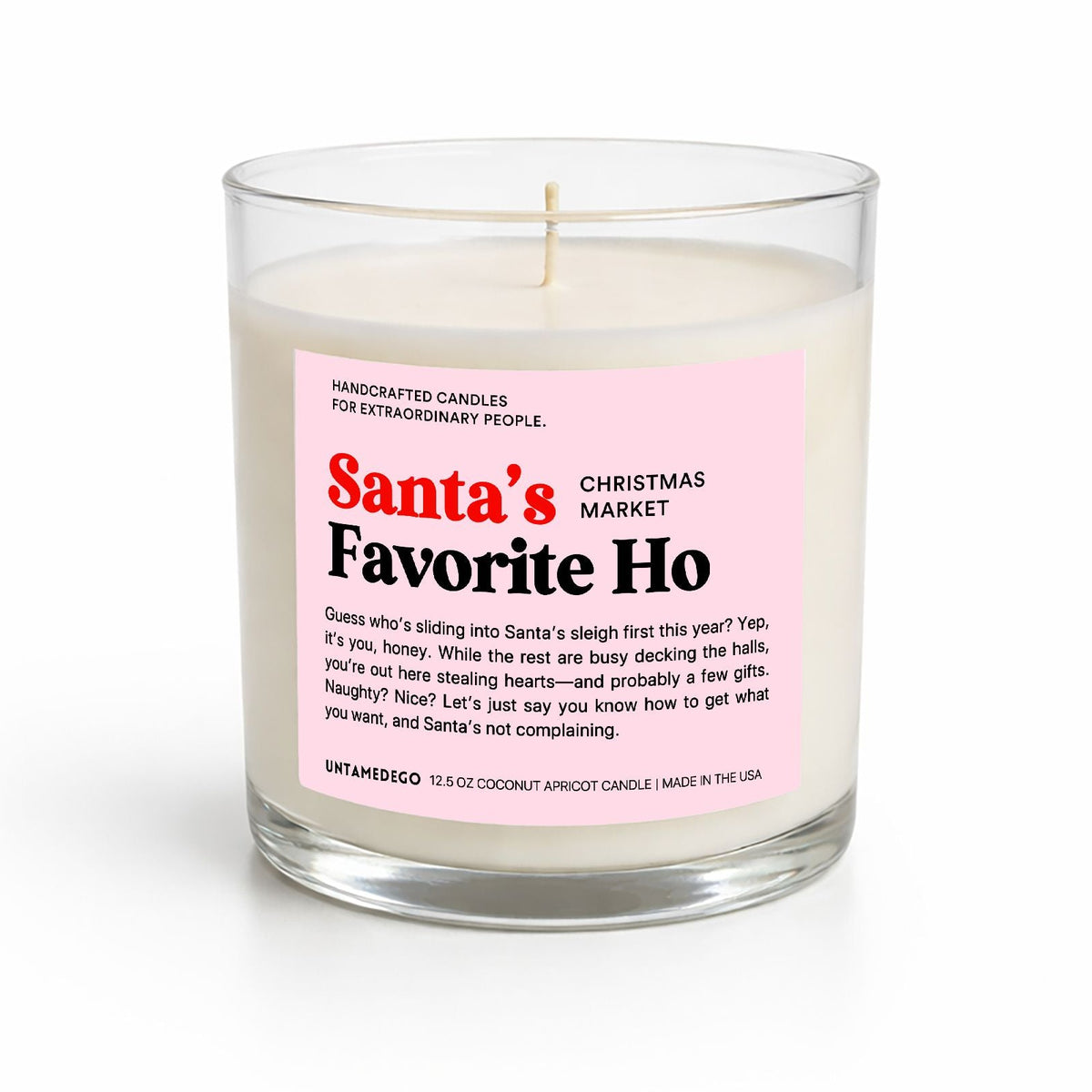 A handcrafted soy candle in a clear glass jar with a wick, featuring a pink label that reads 'Santa's Favorite Ho' and 'Christmas Market' by Unsanded. The candle is photographed on a clean white background with a soft shadow.