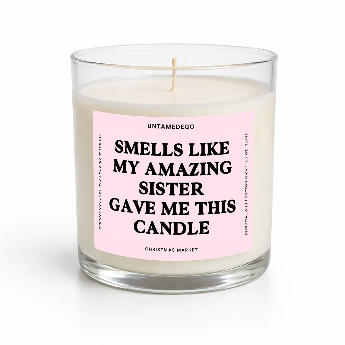 A single-wick soy candle in a clear glass jar with a light pink label that reads 'SMELLS LIKE MY AMAZING SISTER GAVE ME THIS CANDLE' by Untamedgo, on a white background.