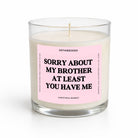 A single-wick soy candle in a clear glass jar with a light pink label that reads 'SORRY ABOUT MY BROTHER AT LEAST YOU HAVE ME' in bold black text. The brand name 'UNTAMEDEGO' is visible at the top of the label.