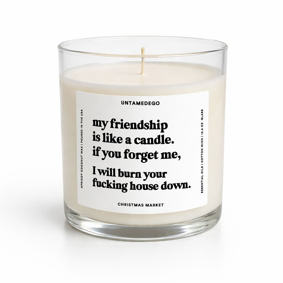 A clear glass jar candle with white wax and a white label featuring black text. The label reads 'UNTAMEDEGO my friendship is like a candle.