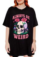 Graphic t-shirt with skull, flowers, and mushrooms design and text saying always be weird
