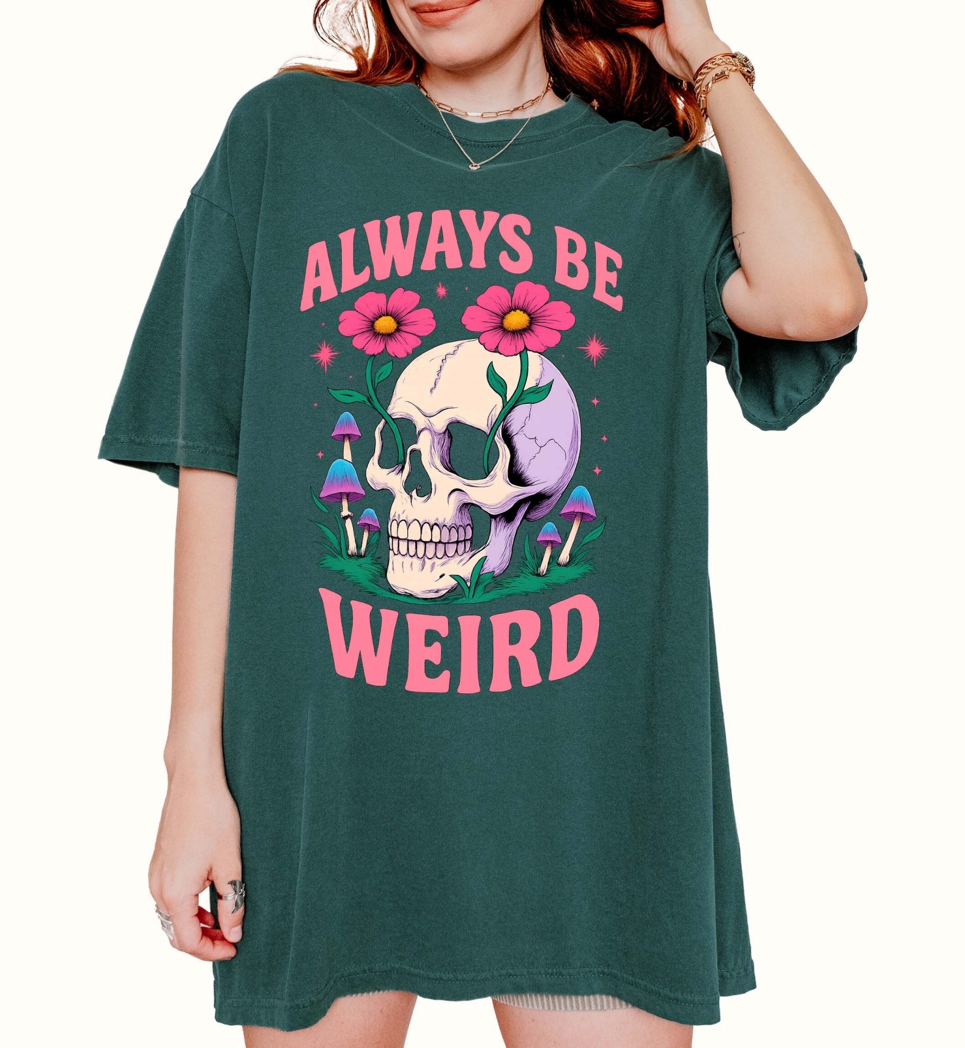 Graphic t-shirt with skull, flowers, and mushrooms design and text saying always be weird