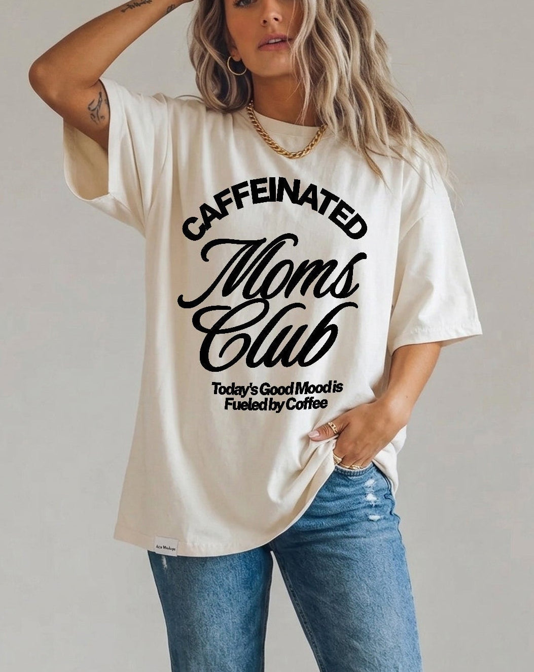 Woman wearing a 'Caffeinated Moms Club' t-shirt and ripped jeans against a plain background