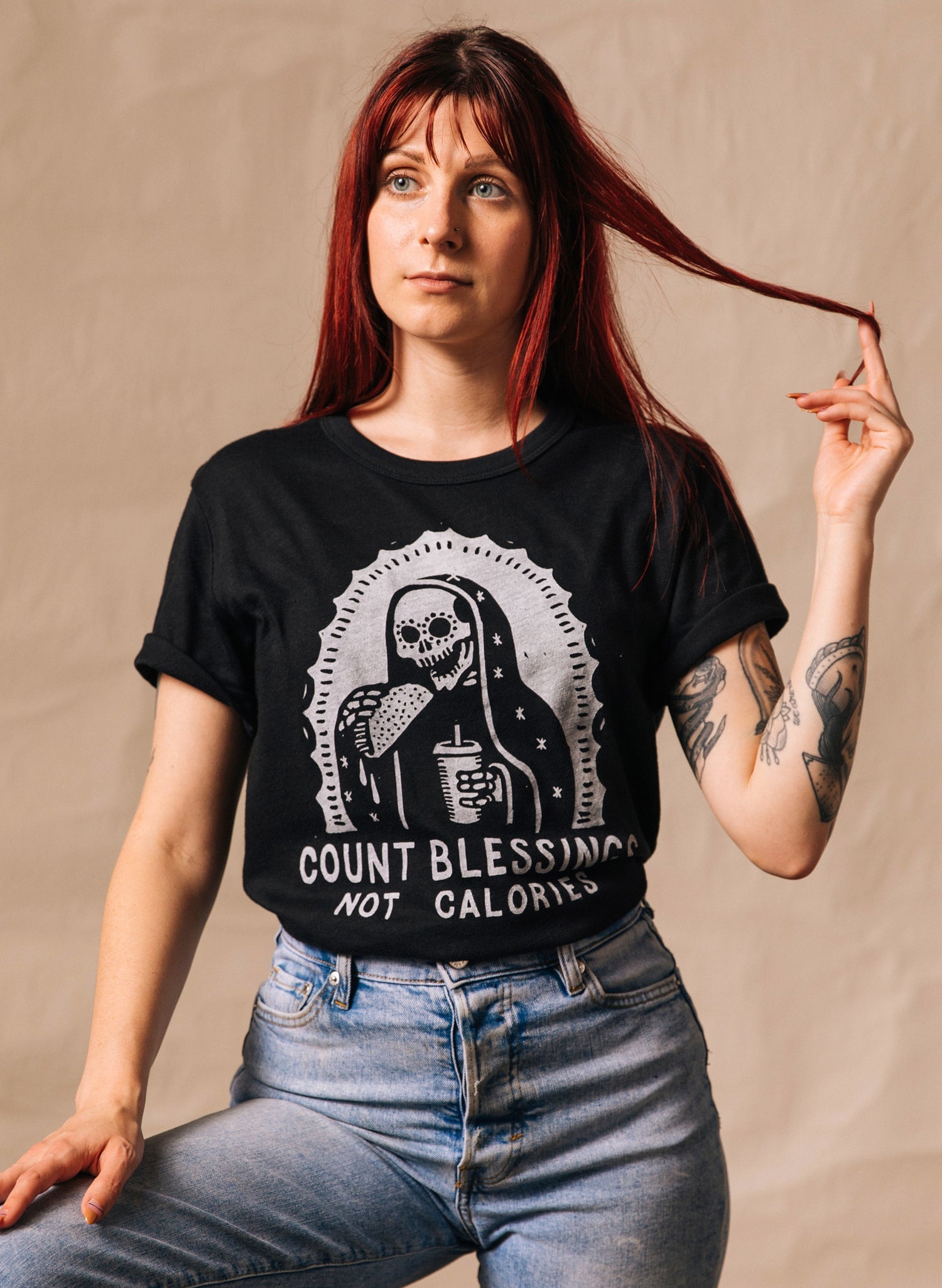 Person wearing a black t-shirt with a graphic design and text, sitting against a beige background