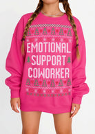A bright pink crewneck sweatshirt with a festive fair isle pattern and the text 'EMOTIONAL SUPPORT COWORKER' in white, worn by a model with braided hair.