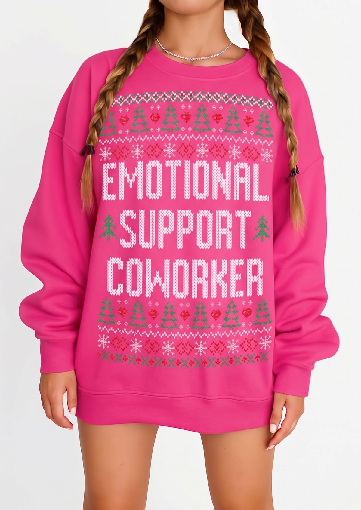 A bright pink crewneck sweatshirt with a festive fair isle pattern and the text 'EMOTIONAL SUPPORT COWORKER' in white, worn by a model with braided hair.