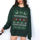 A woman wearing a dark green crewneck sweatshirt with a festive Christmas pattern featuring reindeer, snowflakes, and the text 'EXCEEDING EXPECTATIONS' in white and red.