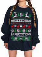 A person wearing an oversized navy crewneck sweatshirt with a festive Christmas sweater print featuring the words 'EXCEEDING EXPECTATIONS' in white, with green and red holiday motifs including reindeer, trees, snowflakes, and gift boxes.